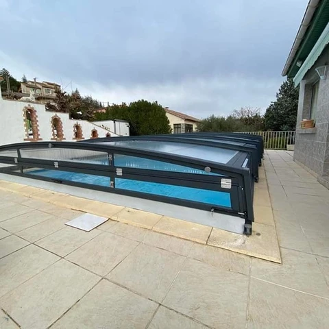 Piscine extérieure résidentielle équipée d'un abri télescopique bas en aluminium et polycarbonate, sur terrasse carrelée