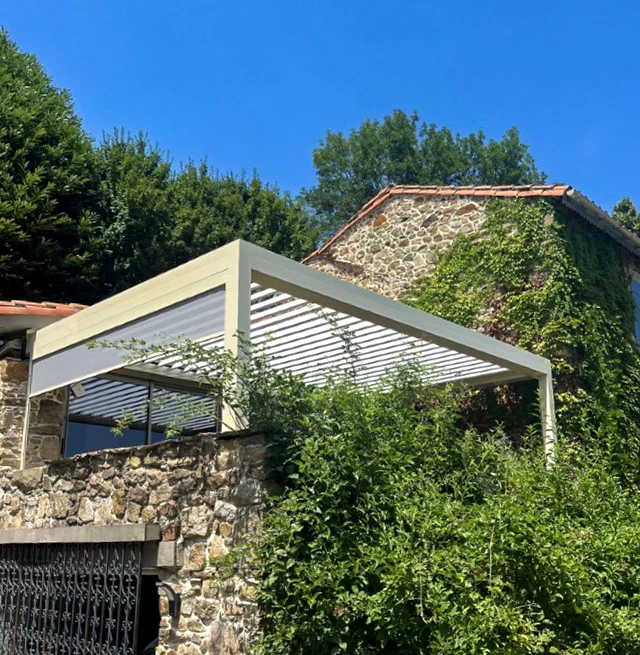 Terrasse extérieure avec pergola bioclimatique à lames orientables blanches, structure métallique moderne installée sur mur en pierre naturelle