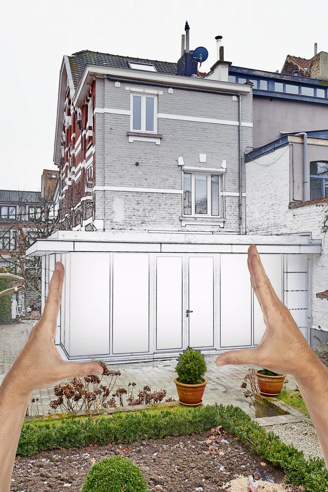 Scène extérieure montrant des mains encadrant un garage préfabriqué blanc dans un jardin résidentiel