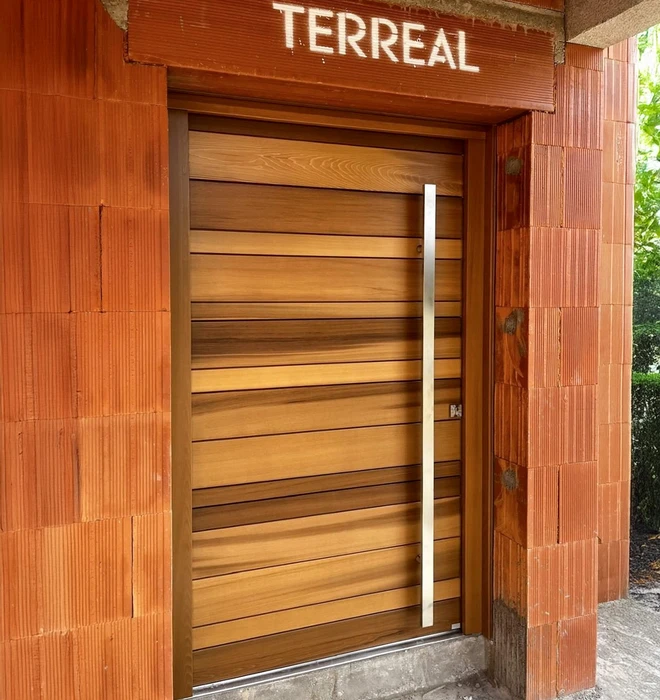 Véranda moderne à structure métallique anthracite avec grandes baies vitrées, adossée à maison traditionnelle aux murs crépis beiges et toiture tuiles canal