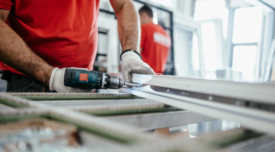 Un menuisier focalisé utilise un pistolet à colle pour coller un panneau de bois à un cadre en bois dans un atelier, démontrant un savoir-faire et une précision dans le travail du bois