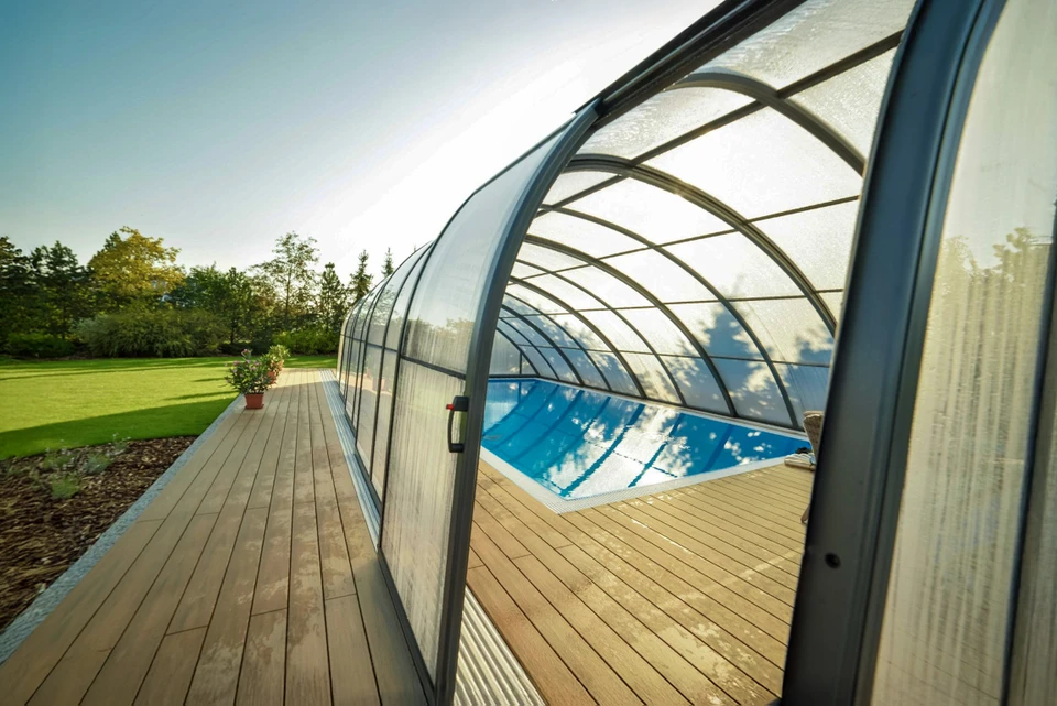 Espace extérieur avec piscine entourée de barrière vitrée, terrasse en bois exotique et pergola en bois