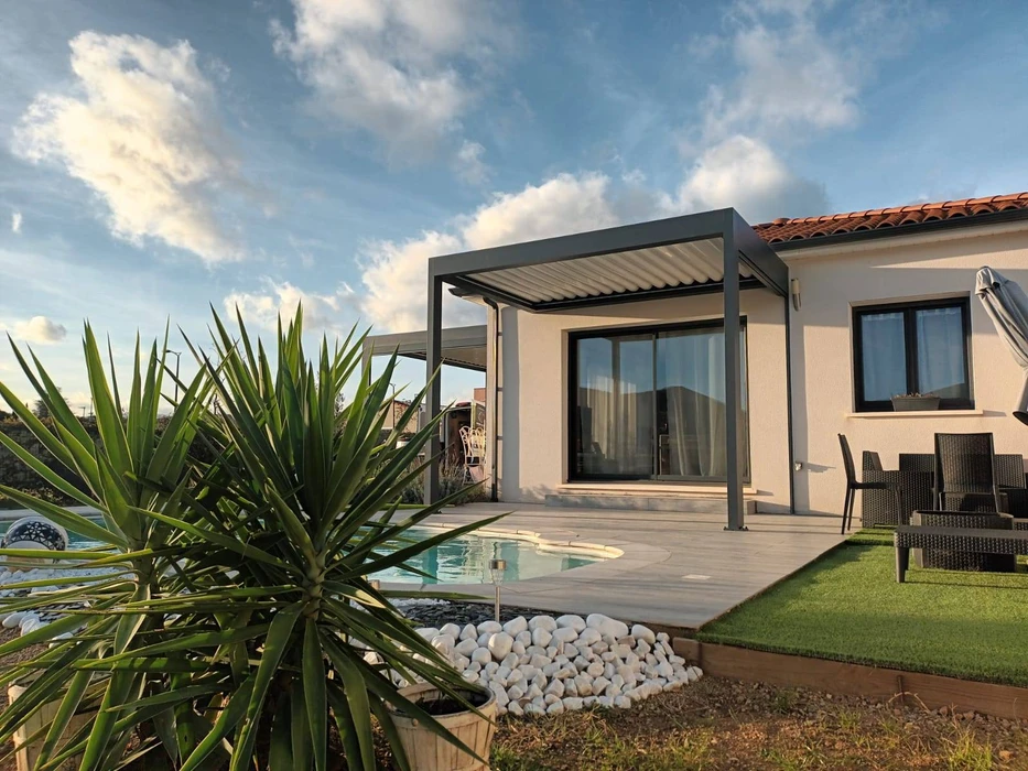 Terrasse extérieure couverte d'une pergola bioclimatique à lames orientables blanches, structure aluminium beige