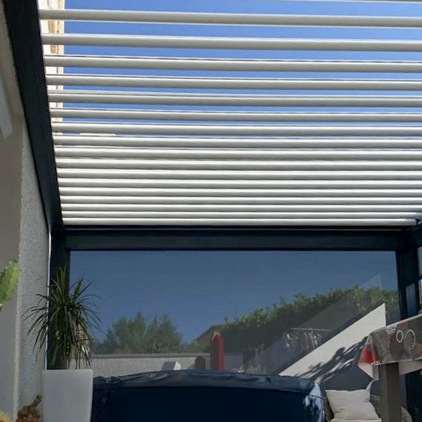 Terrasse extérieure couverte d'une pergola bioclimatique à lames orientables blanches, structure aluminium beige