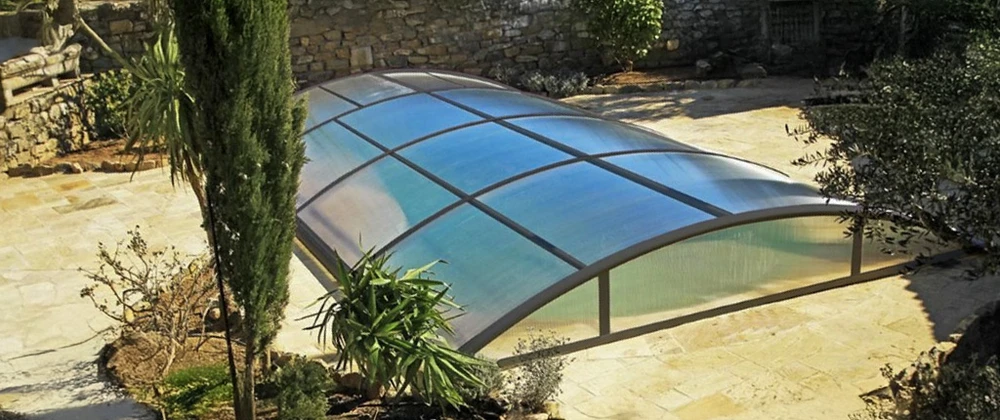 Piscine extérieure résidentielle équipée d'un abri télescopique bas en aluminium et polycarbonate, sur terrasse carrelée
